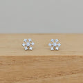 A pair of silver snowflake stud earrings set with small clear stones, resting on a light brown wooden surface against a neutral gray background.