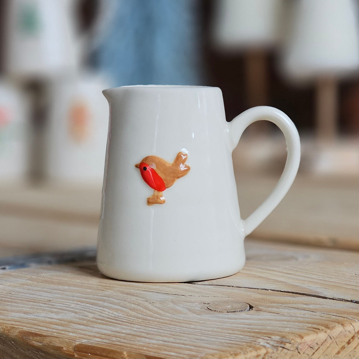 White ceramic mini jug with a robin design on a wooden surface