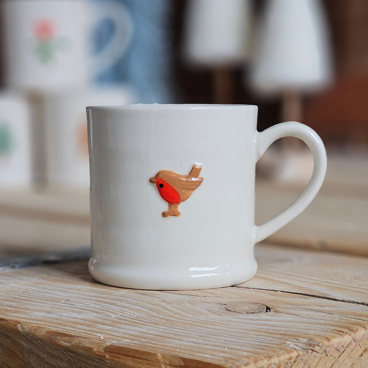 White mug with a small figurine of a bird on the front, displayed on a wooden surface
