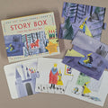 A children's jigsaw puzzle set titled 'STORY BOX' arranged on a neutral beige surface. The set includes a colourful illustrated box and several puzzle pieces showing whimsical fairy tale scenes, including a castle, a king and queen, and characters in a forest.