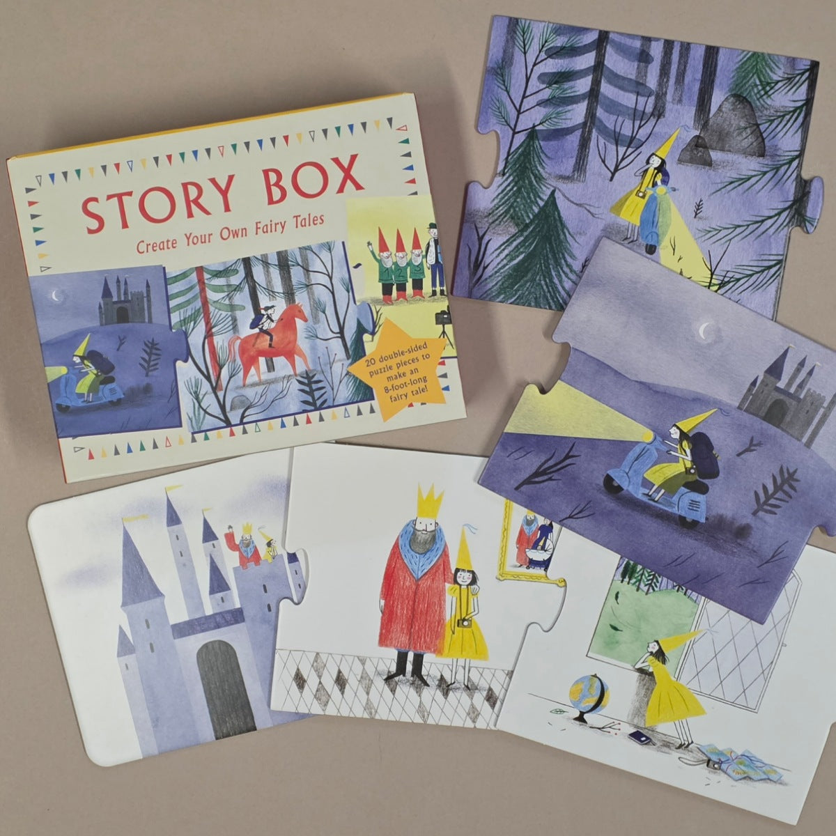 A children's jigsaw puzzle set titled 'STORY BOX' arranged on a neutral beige surface. The set includes a colourful illustrated box and several puzzle pieces showing whimsical fairy tale scenes, including a castle, a king and queen, and characters in a forest.