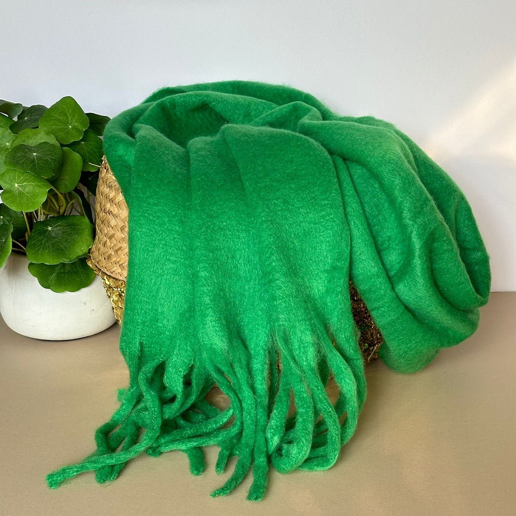 Bright green chunky soft scarf with tassels draped over a woven basket on a neutral background.
