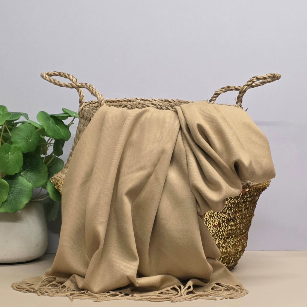 Beige fabric draped over a woven basket with a plant in the background