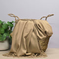 Beige fabric draped over a woven basket with a plant in the background