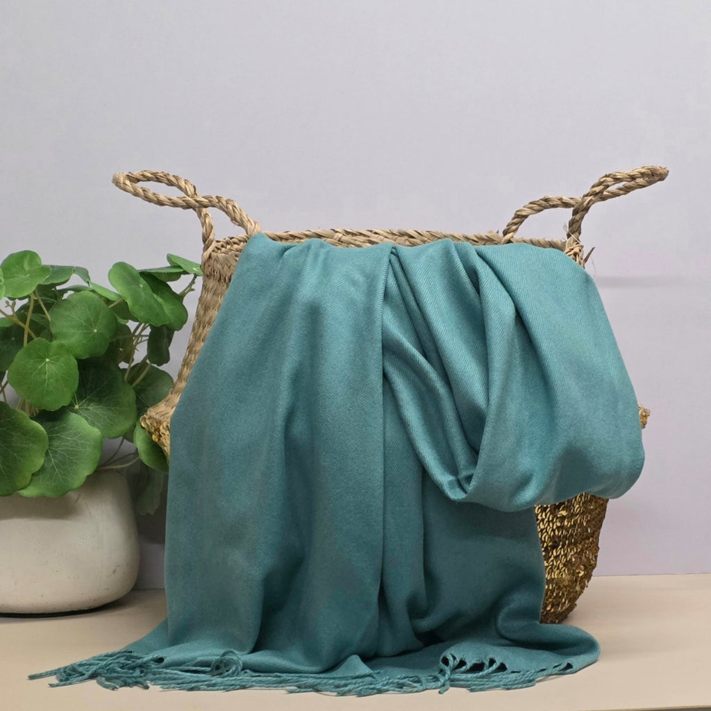 Teal fabric draped over a woven basket with a plant in the background
