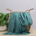Teal fabric draped over a woven basket with a plant in the background