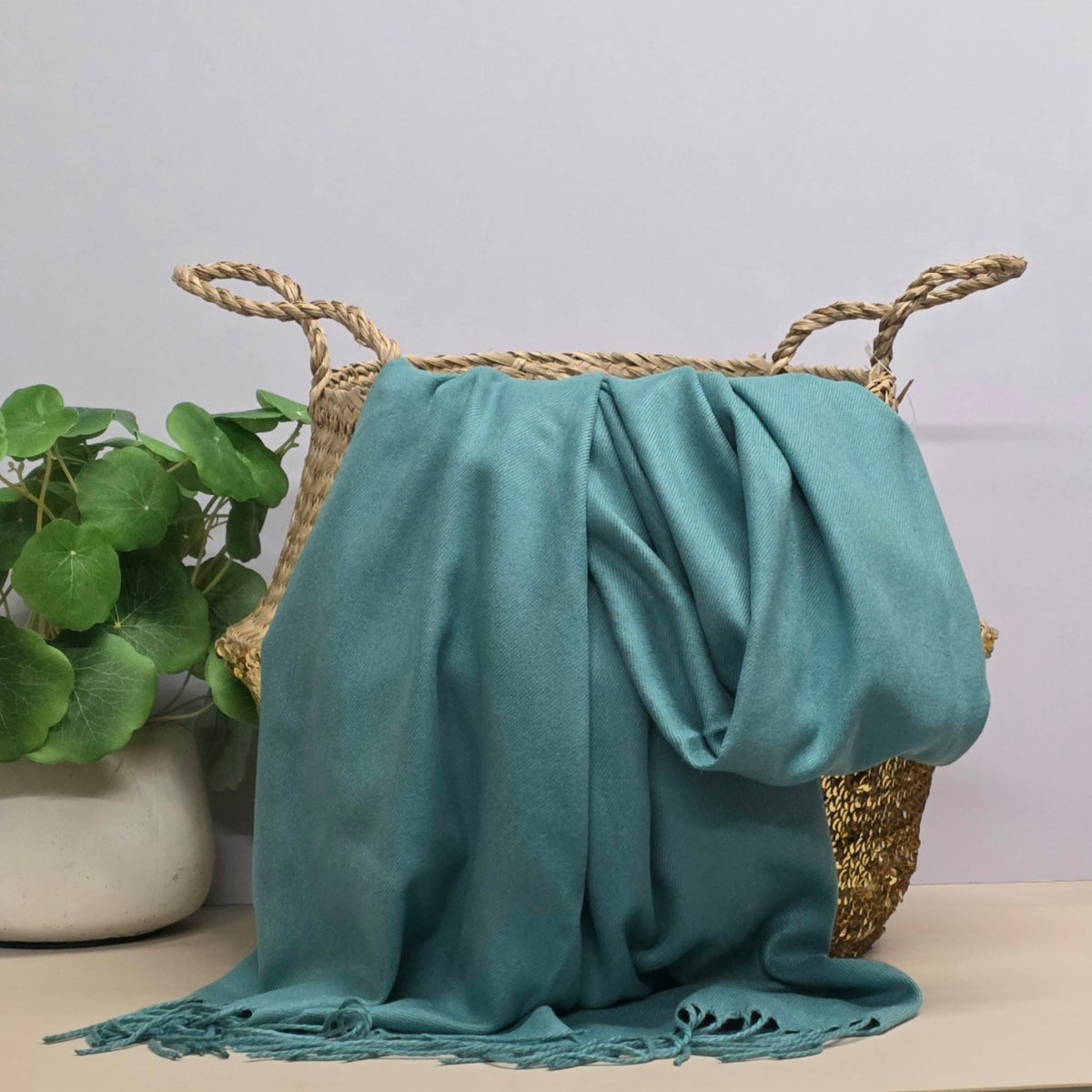 Teal fabric draped over a woven basket with a plant in the background