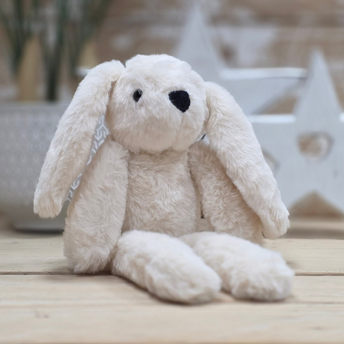 A cream soft fuzzy plush bunny toy, with black eyes and nose, on a wooden surface with a blurred star-shaped object in the background
