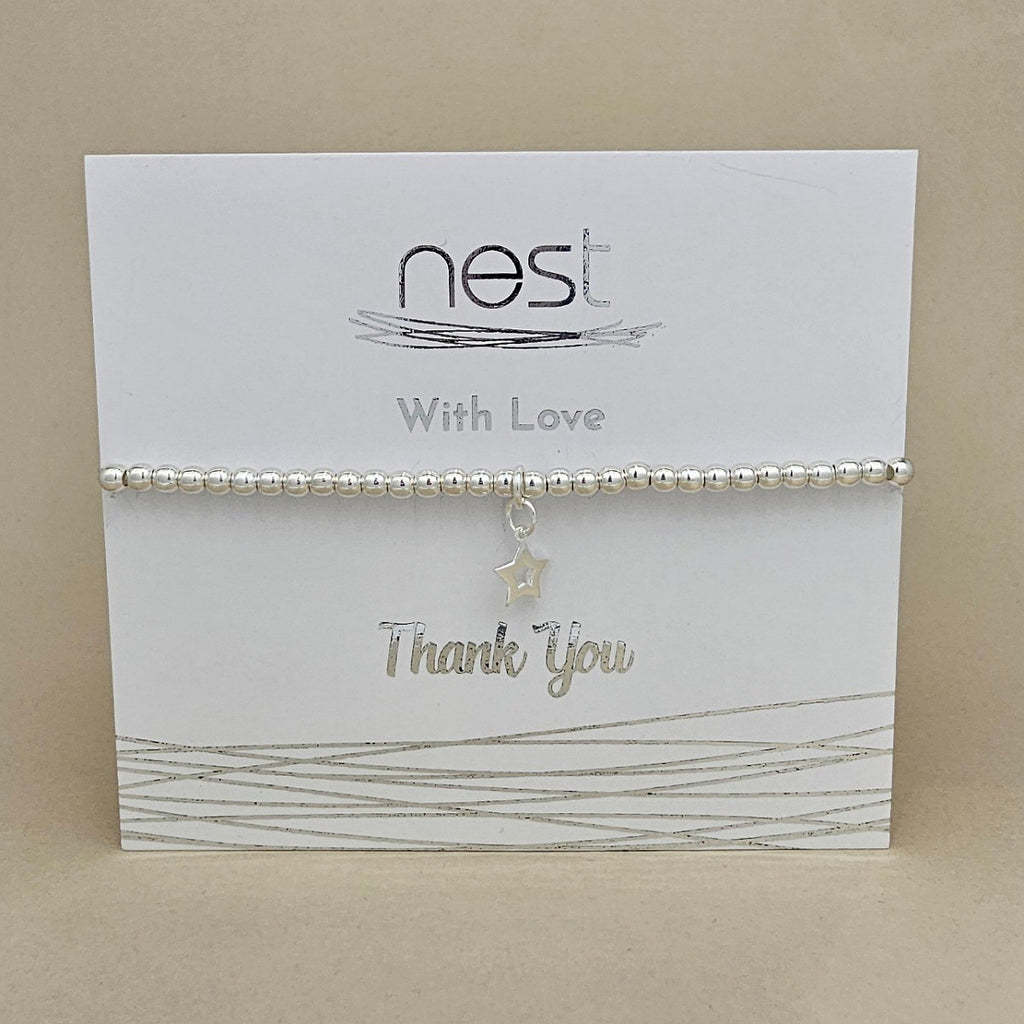 A silver beaded bracelet with a dangling star charm, presented on a white 'nest With Love Thank You' gift card against a beige background.