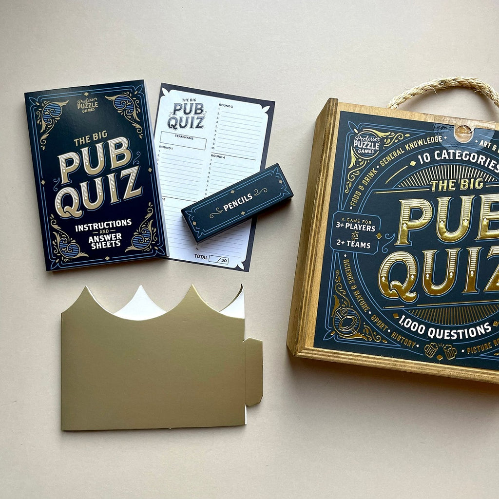 Wooden box with words 'The Big Pub Quiz' game set on a light surface with packaging and information.