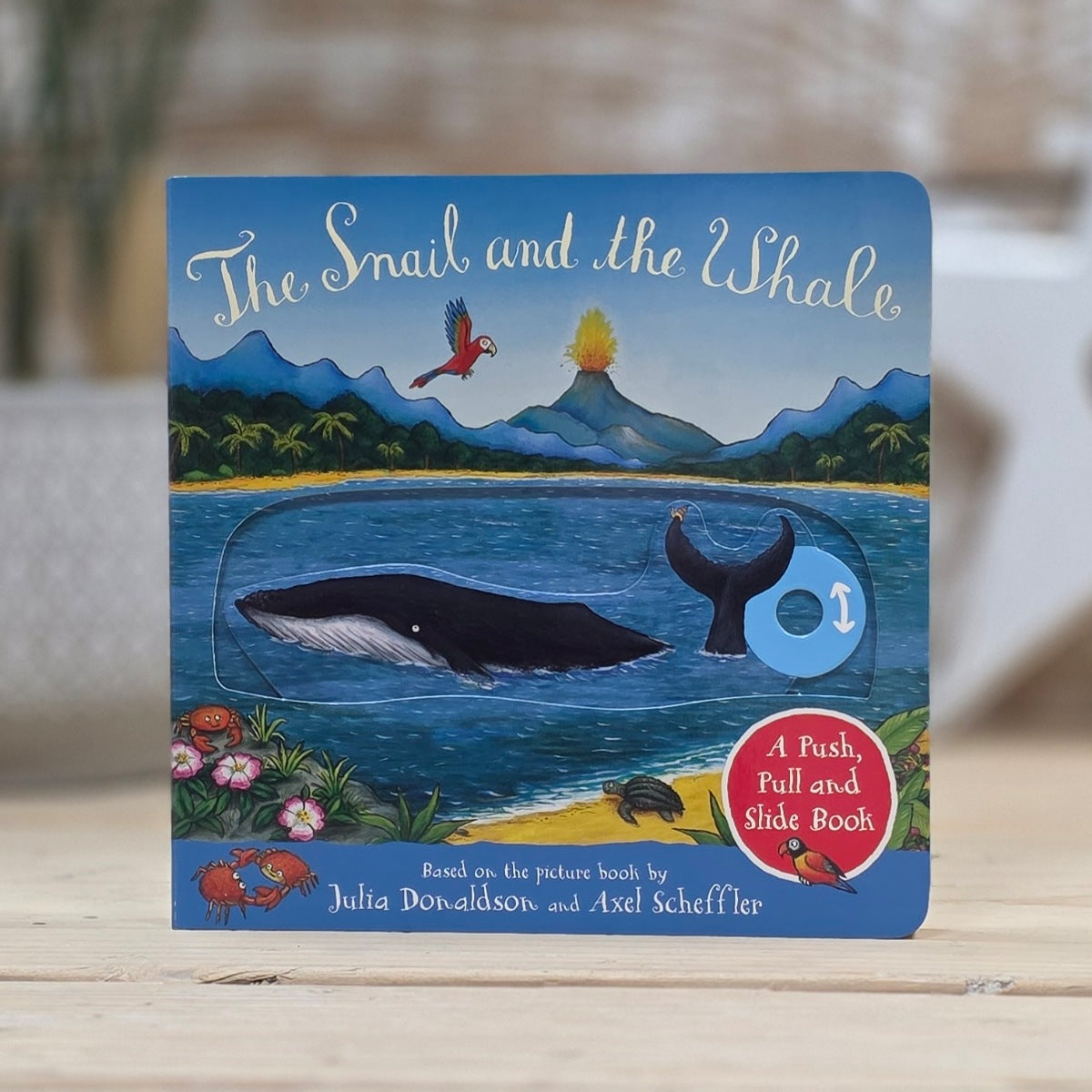 Children's book titled 'The Snail and the Whale' with a whale illustration on a wooden surface.