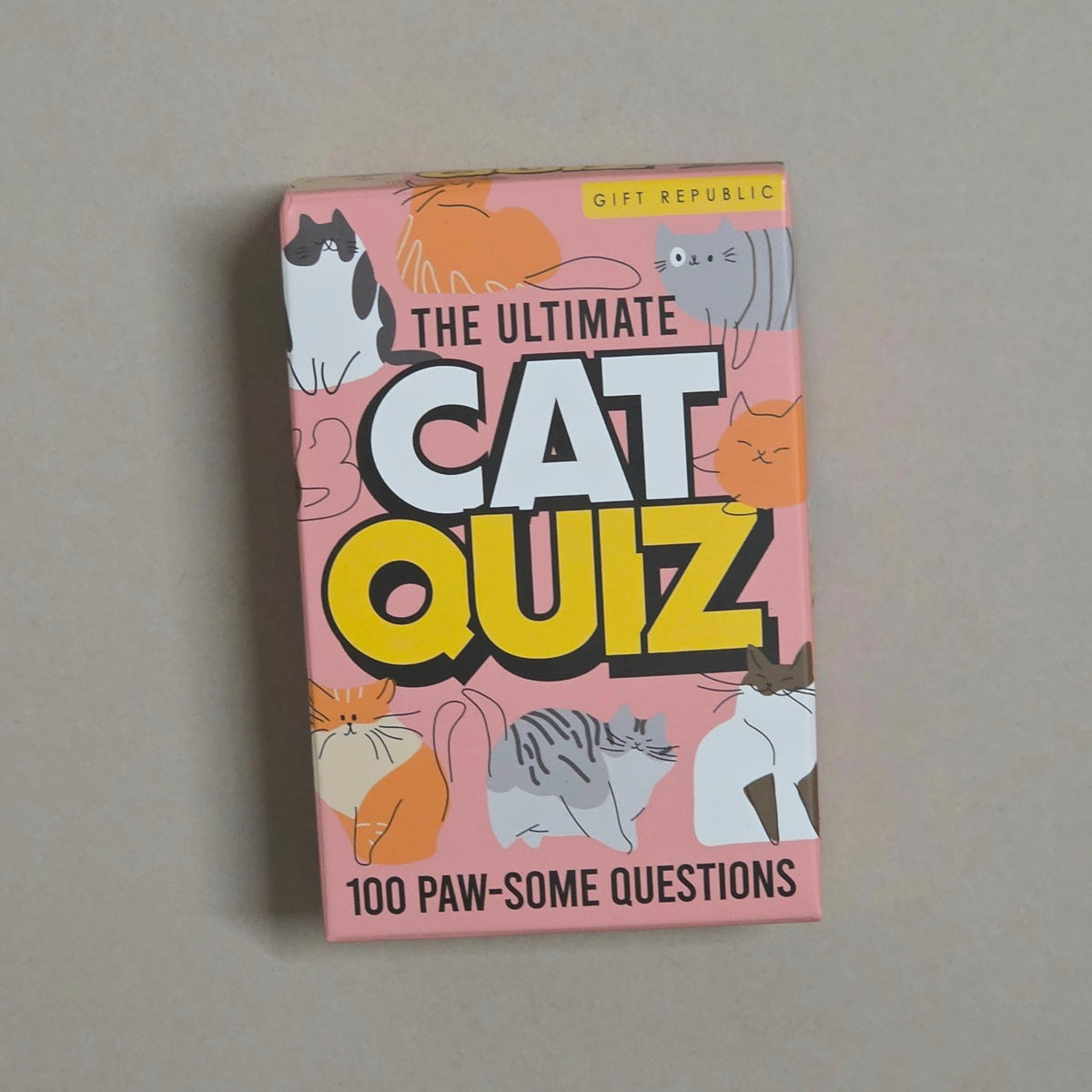 The Ultimate Cat Quiz card deck box by Gift Republic, featuring a pink background with various cartoon cat illustrations and bold yellow and white text, photographed on a neutral gray surface.
