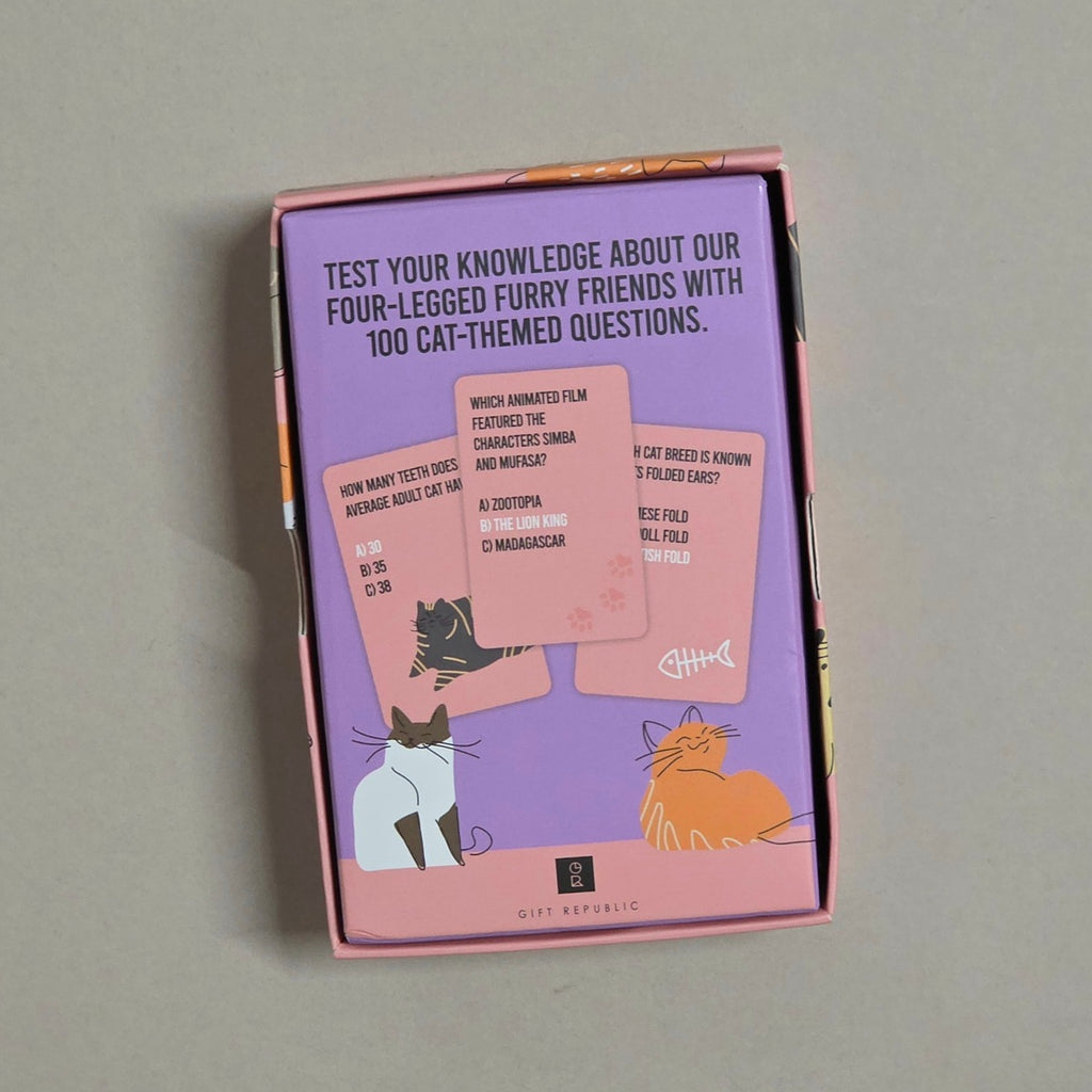 A pink and purple box of Gift Republic cat-themed trivia cards, showing the back of the packaging with sample questions and illustrations of a black cat, white cat, and orange cat on a neutral gray background.