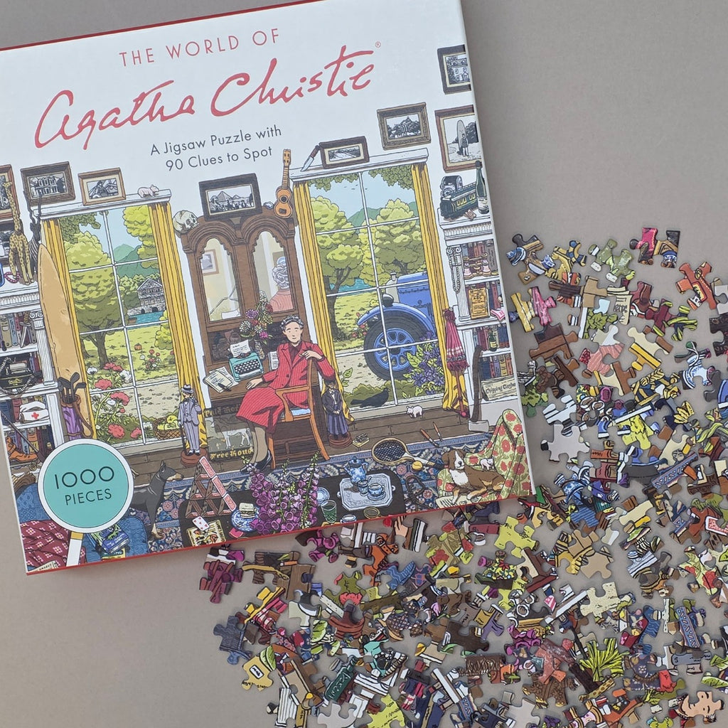 Jigsaw puzzle box titled 'The World of Agathe Christie' with scattered puzzle pieces on a flat beige surface
