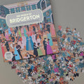 Jigsaw puzzle box titled 'The World of Bridgerton' with scattered puzzle pieces on a flat beige surface
