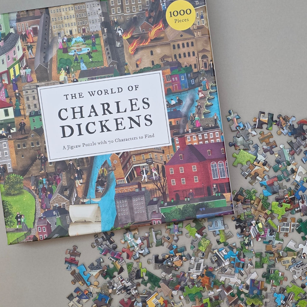 Jigsaw puzzle box titled 'The World of Charles Dickens' with scattered puzzle pieces on a flat beige surface
