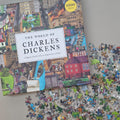 Jigsaw puzzle box titled 'The World of Charles Dickens' with scattered puzzle pieces on a flat beige surface
