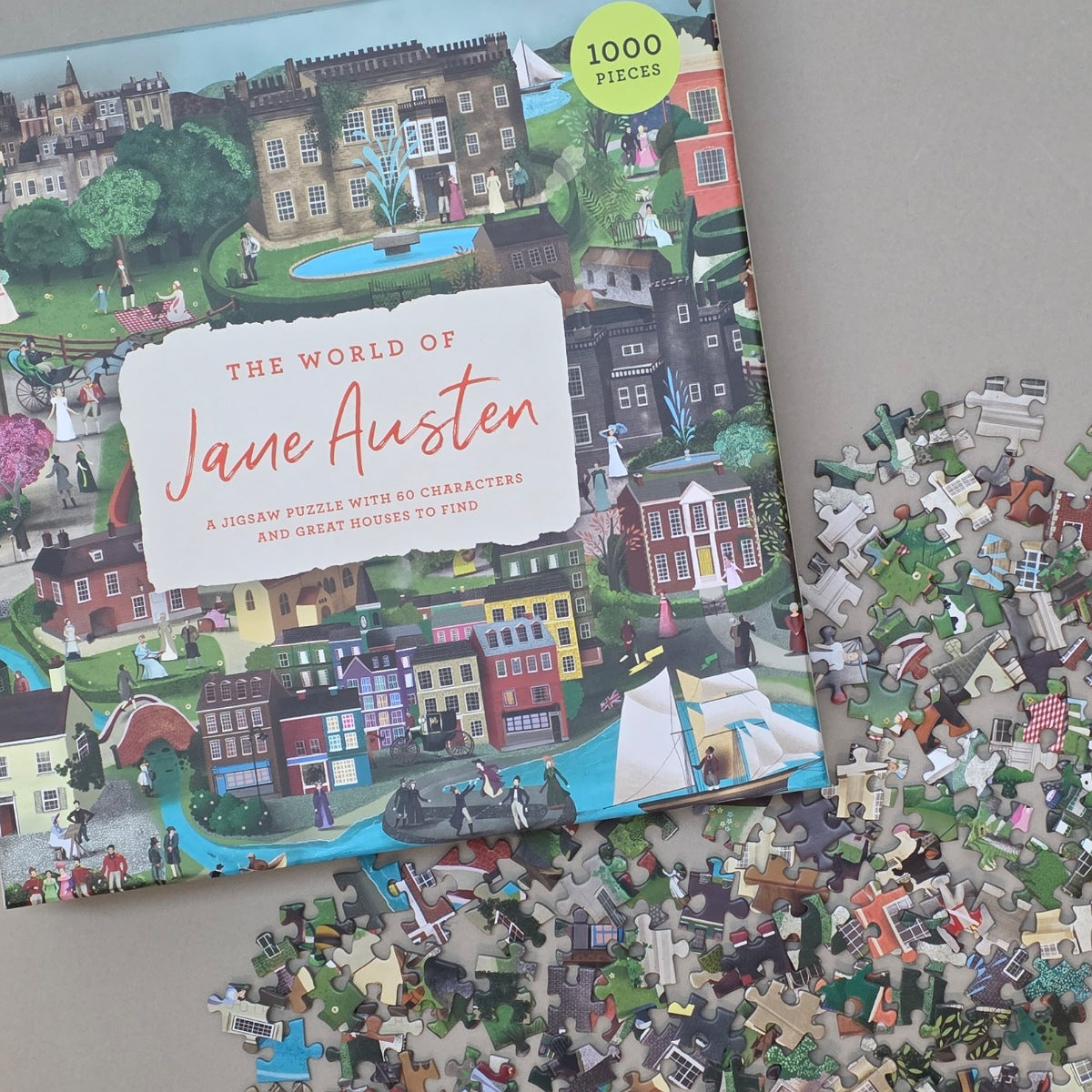Jigsaw puzzle box titled 'The World of Jane Austen' with scattered puzzle pieces on a flat beige surface

