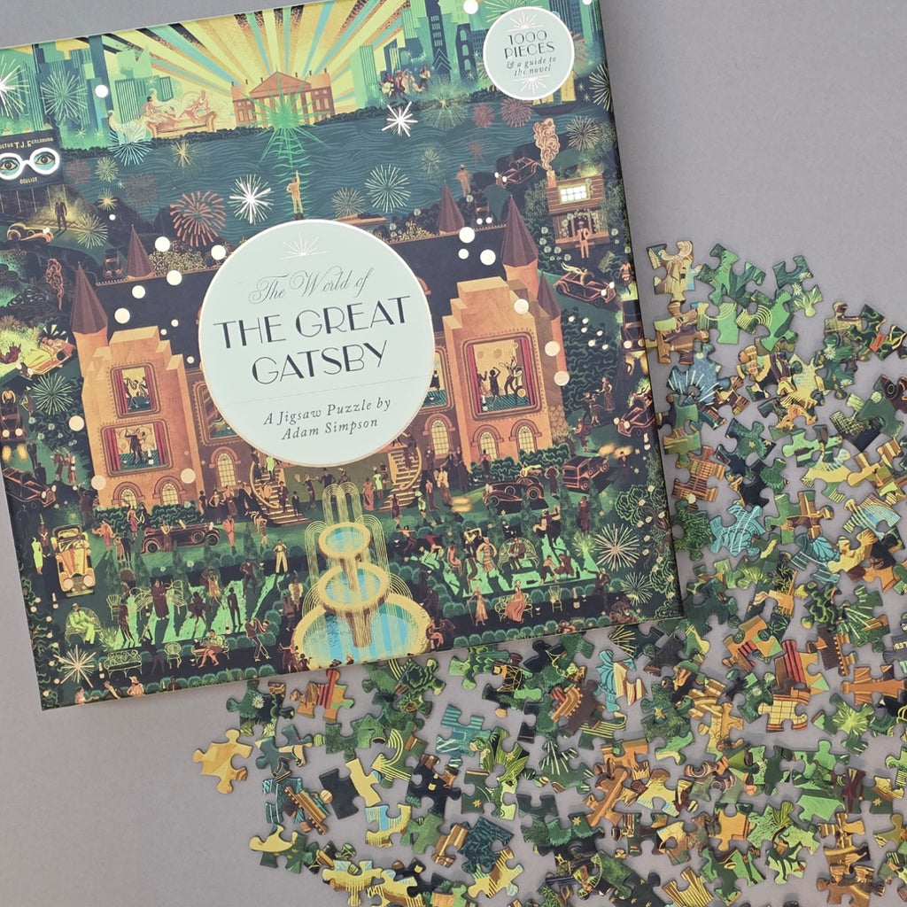 Jigsaw puzzle box titled 'The Great Gatsby' with scattered puzzle pieces on a flat beige surface