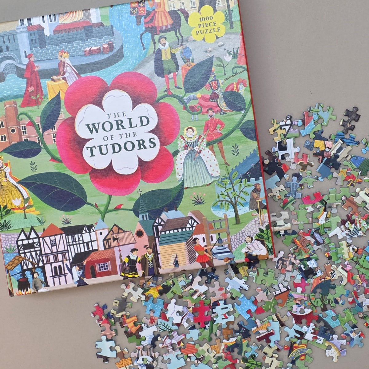 Jigsaw puzzle box titled 'The World of the Tudors' with scattered puzzle pieces on a flat beige surface
