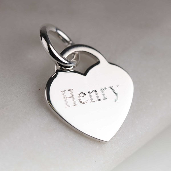 A polished silver heart-shaped pendant charm engraved with the name 'Henry', resting on a light gray textured surface.