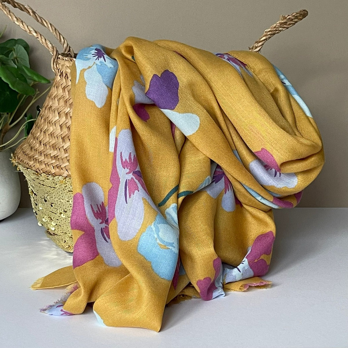 Mustard fabric with colourful viola flower patterns in purple, pink, light blue and white draped over a woven basket on a light surface.