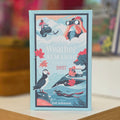 A hardcover book titled 'Weather Almanac: A Guide to 2027' by Zoe Johnson, standing upright on a wooden surface with a blurred indoor background.