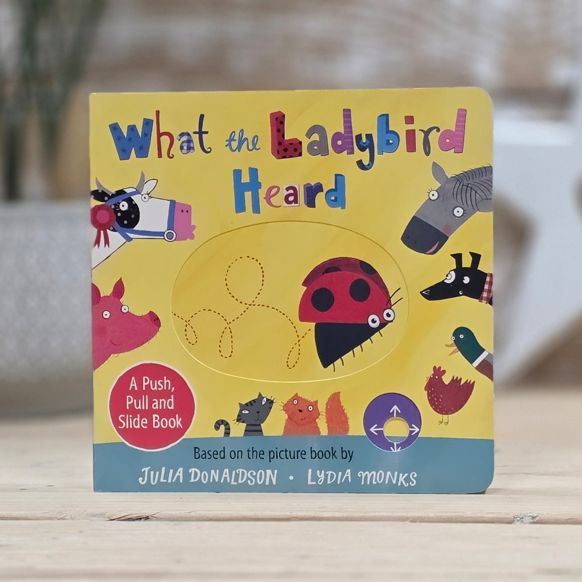 Children's book titled 'What the Ladybird Heard' with colorful illustrations on a wooden surface.