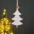 Wooden hanging tree decoration in white with gold dots, a star to the top with a gold bell.  Hanging with a dark background a blurred out Christmas tree.