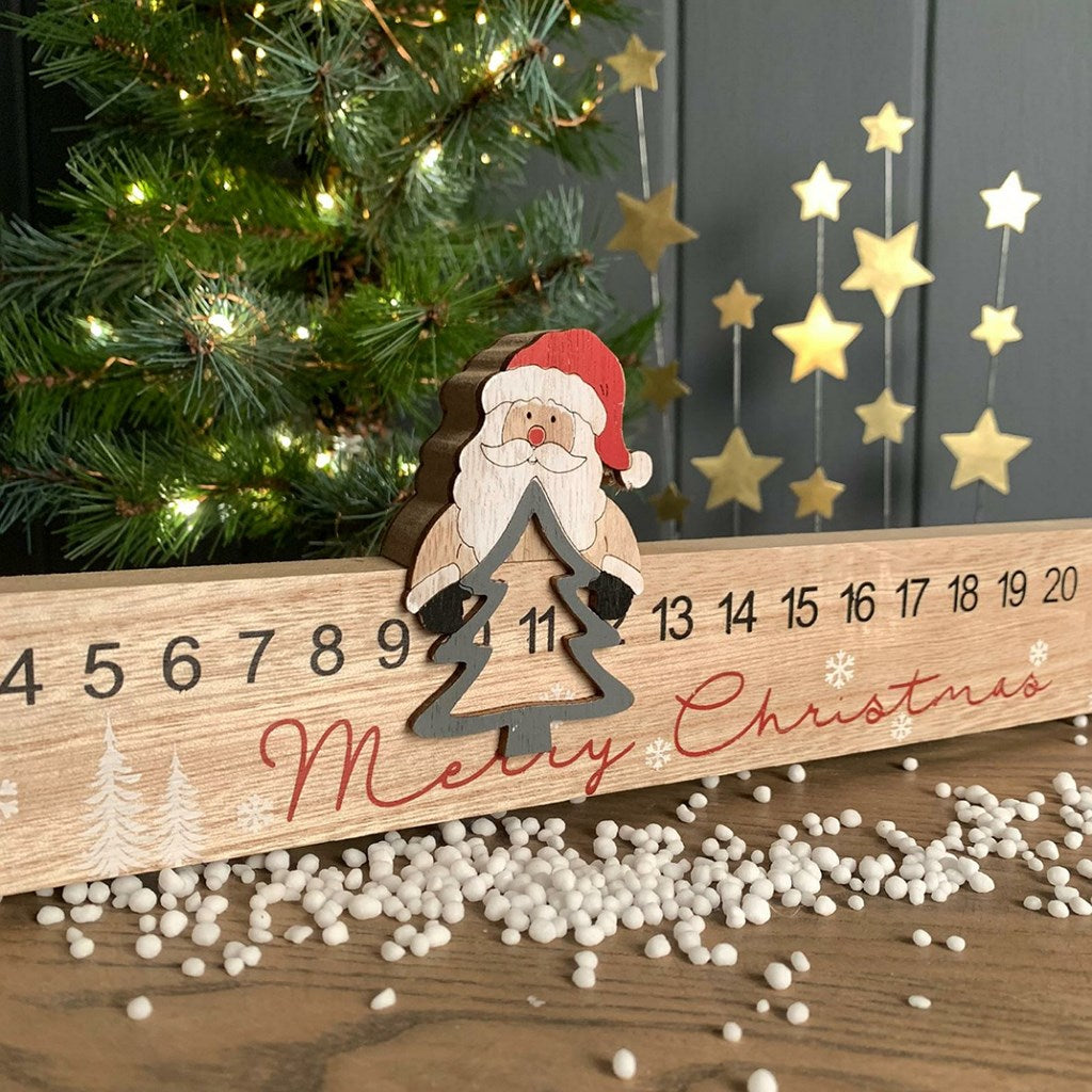 Wooden Christmas countdown calendar with moveable Santa Claus decoration, tree cutout sitting on top, and festive decorations.