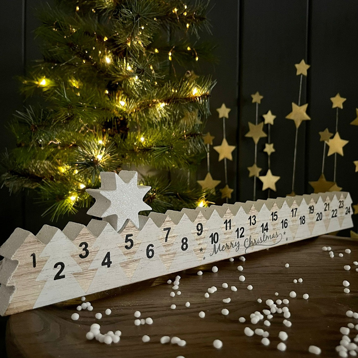 Wooden Christmas countdown calendar with decorative stars and tree in the background