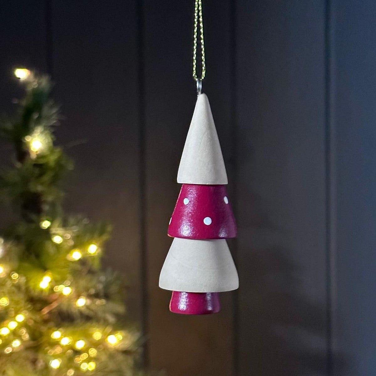 Decorative wooden hanging tree ornament with white and red design, blurred Christmas tree in the background.