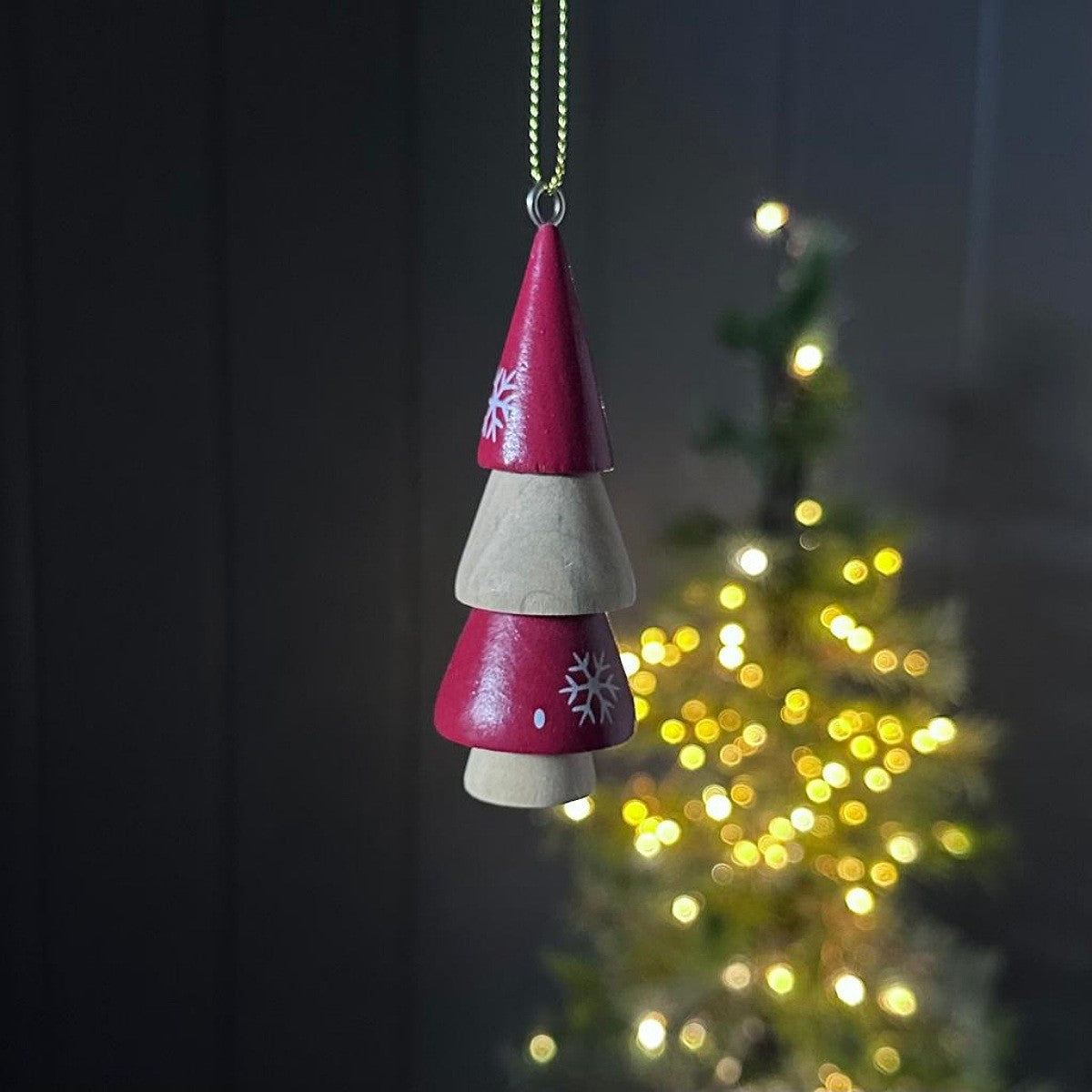 Decorative wooden hanging tree ornament with white and red design, blurred Christmas tree in the background.