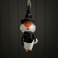 Hanging fox decoration dressed as a witch holding a magazine with a black hat and glasses on a dark background