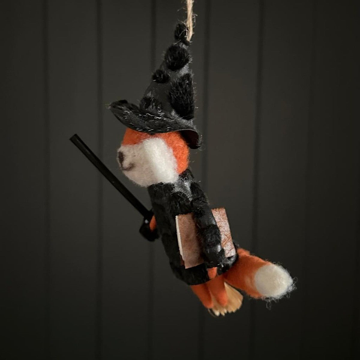 Hanging fox decoration dressed as a witch with a broomstick on a dark background