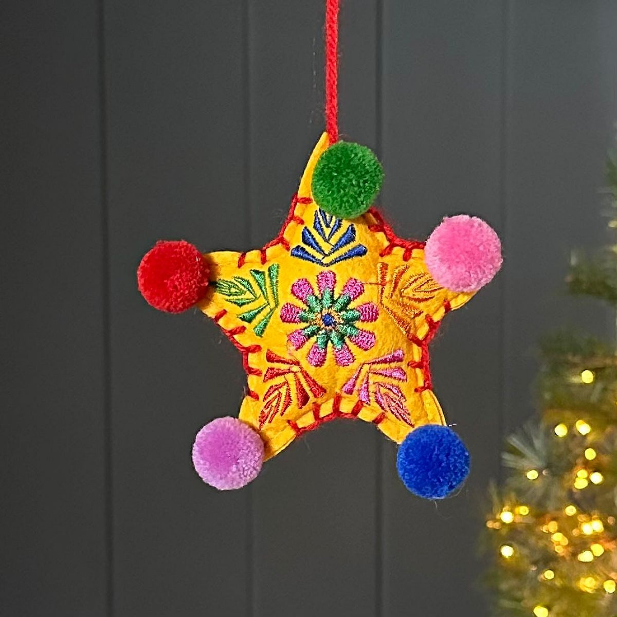 Colourful star-shaped hanging decoration with multi coloured pom-poms on a dark background