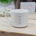 White ceramic mug with the wording 'pause' inside the mug land three love hearts on the front, on a wooden surface with flowers and a box in the background